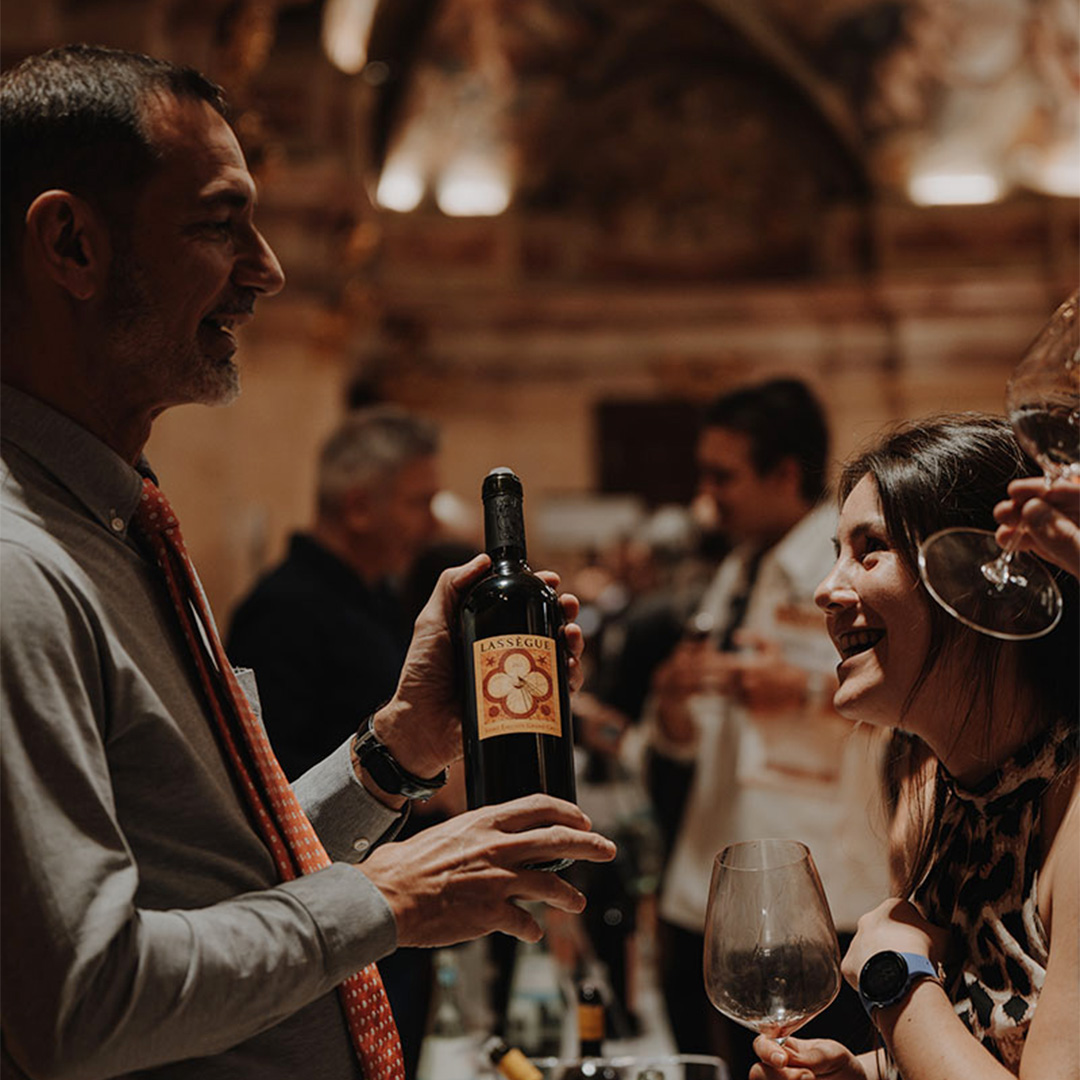 Portfolio Tasting 2024 Ein Vertreter von Chateau Lassegue präsentiert eine Flasche Lassegue interessierten Kunden auf einer Weinmesse